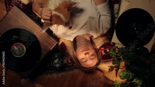 Woman relaxing on the floor with her dog, listening to vinyl records in warm sunlight, enjoying a peaceful moment