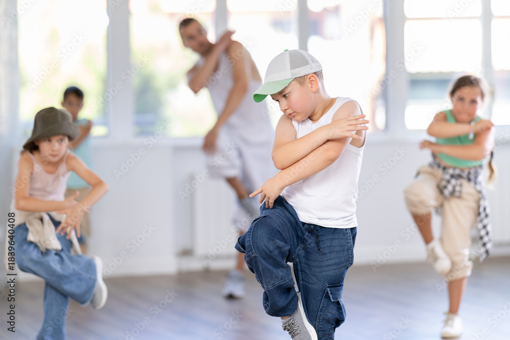 Obraz premium Preteen boy performing hip hop dance moves, showcasing skills and concentration, during group class for kids led by young male instructor in street dance studio