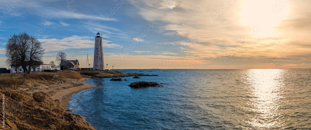 Fototapeta premium The historic New Haven Lighthouse, aka Five Mile Point Light, a 70-foot sandstone sentinel built in 1847, at the entrance to New Haven Harbor, in East Rock, New Haven, Connecticut, USA, at sunset