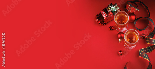 Top view of whiskey glasses with toy car, baubles, ribbon and space for text on red background. Holiday mockup layout.