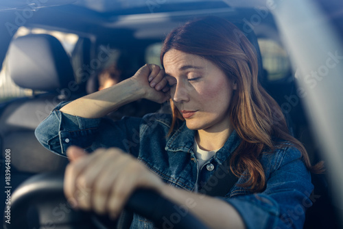 Woman sits in car looking worried and tired