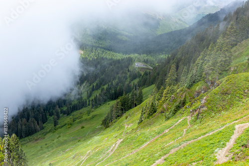 Фотография Sauk Mountain Trail winds its way up a steep slope with multiple switchbacks as clouds roll in beginning to obscure the view