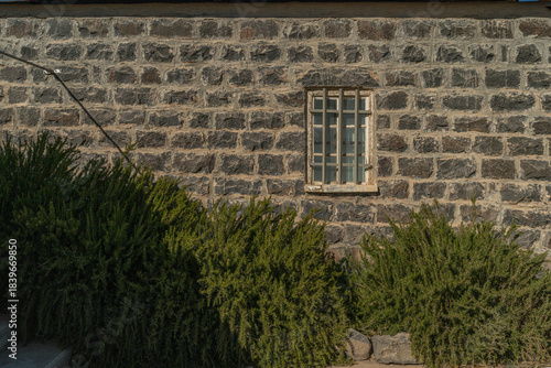 Window in Azraq's old hospital: Sunlight through historic wood frame set in thick stone walls of the black basalt structure in Jordan.