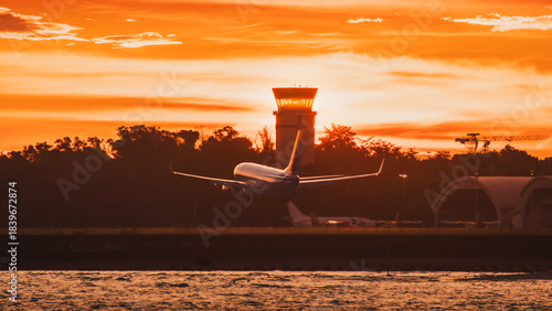 Jet Airplane Landing at Sunset Near Control Tower