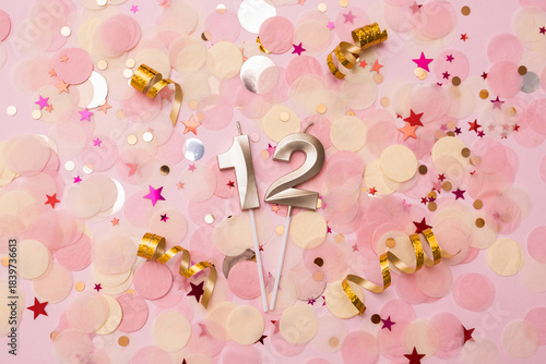 Golden wax candles in the shape of the number 12 on confetti background. Happy birthday concept. Selective focus