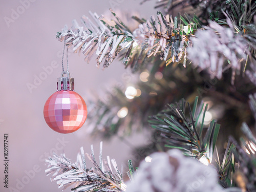Close-up of shiny pink Christmas ball hanging on Christmas tree with Christmas light background