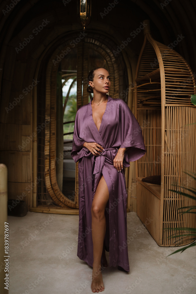 Fototapeta premium A woman in a purple robe stands in a bamboo corridor with handcrafted walls and tropical greenery in the background