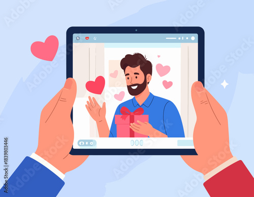 Hands holding a tablet displaying a video call with a bearded man holding a gift box and surrounded by hearts, symbolizing online dating or a virtual celebration.