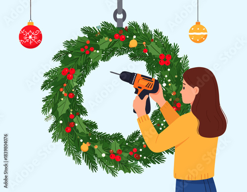 A woman uses a drill to hang a large, festive Christmas wreath. A creative and handy approach to holiday decorating.