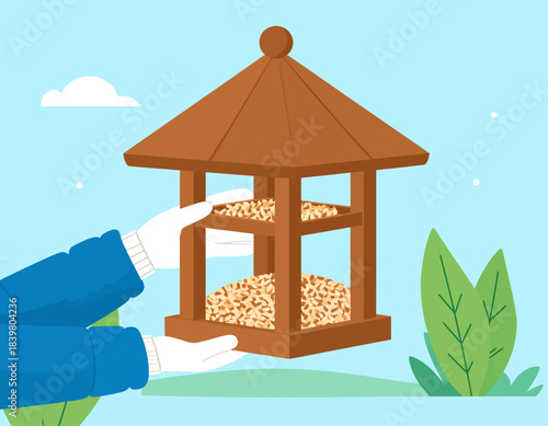 Hands in winter gloves hold a wooden bird feeder filled with seeds. An illustration of kindness and caring for wildlife during colder months.
