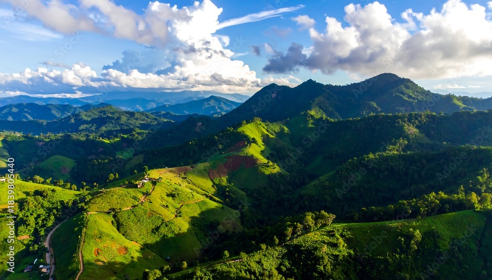 Fototapeta premium Aerial view captures rolling green hills under a bright, partly cloudy sky