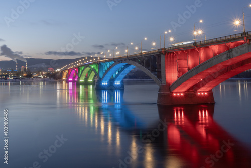 The symbol of the city of Krasnoyarsk is an arched communal bridge over the Yenisei River in a multicolored illumination at night. Beautiful cities of Russia in the center of Siberia. High quality