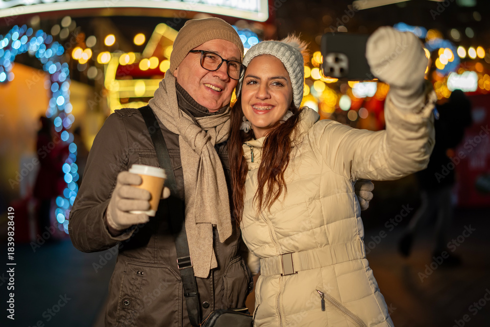 Fototapeta premium Couple enjoying festive christmas market selfie together