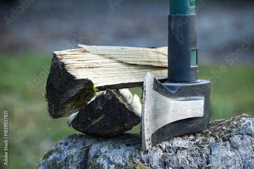 Axe and firewood on a tree stump, ready for chopping, with a blurred background.