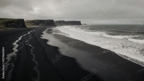 A black sand beach under a gray sky with cliffs and waves crashing