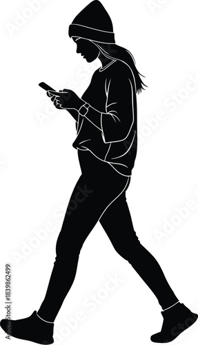 Silhouette of a young woman wearing a beanie and casual clothes walking while deeply focused on her mobile phone screen