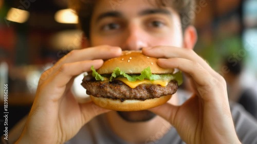 Close-up of a happy young man about to take a bite out of a delicious, freshly made hamburger with cheese, lettuce, and savory patty