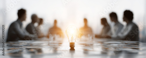 Bright light bulb glowing on table with blurred business people brainstorming in background