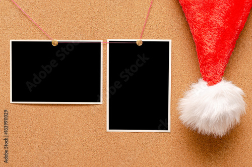 Blank photos are pinned to the board. Santa's hat on a cork board.