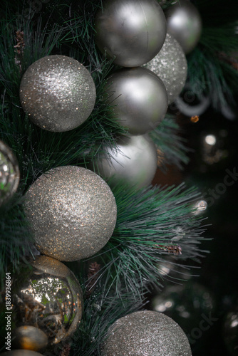 Silver and glittery Christmas ornaments adorn a lush green tree, creating a festive holiday display.