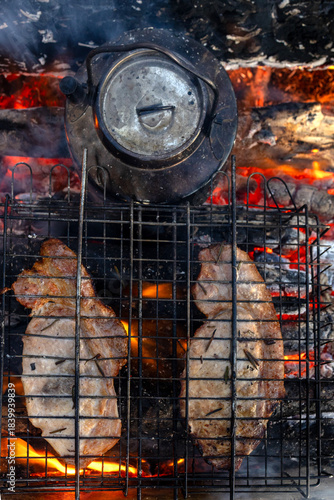 Grilling steaks over a campfire in the forest.