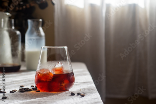Cold brew coffee in a clear glass with ice on a table covered with a natural linen tablecloth.