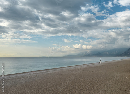 Fototapeta Naklejka Na Ścianę i Meble -  Quiet Konyaalti beach with lifeguard tower under dramatic sunset sky
