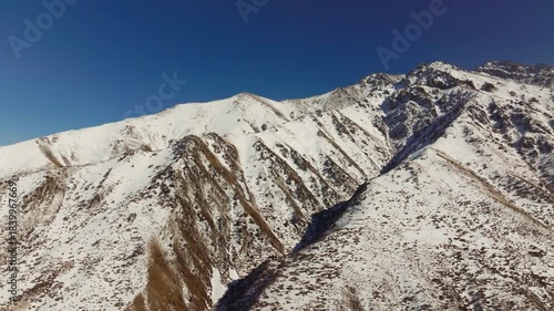 Aerial view captures vast snow-capped mountains in Kyrgyzstan under a clear blue sky. Serene winter landscape evokes feelings of wild beauty and cold tranquility.