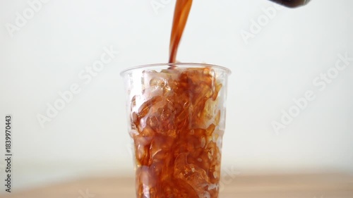 4K Close-up of iced coffee being poured into clear plastic cup filled with ice.