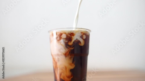 4K Close-up milk Pouring into Iced black Coffee.