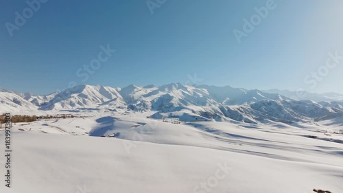 Aerial view captures majestic snow-covered field with mountains in the background. Boom down camera movement.