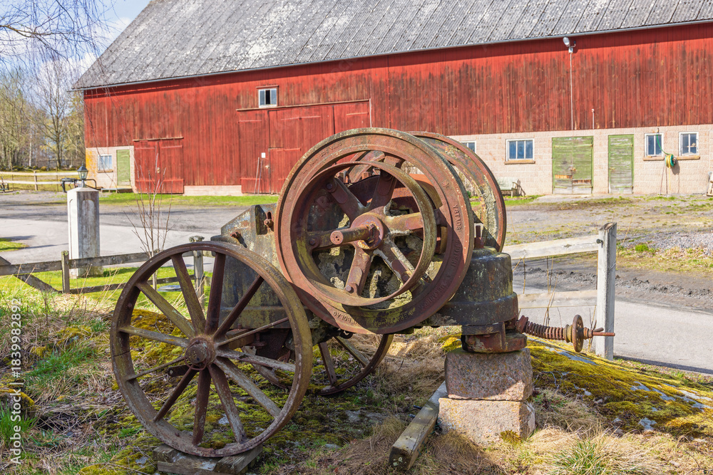 Fototapeta premium Old rusty rock crusher by a red barn in the countryside