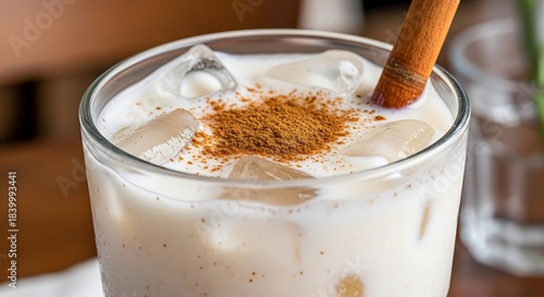 Refreshing Iced Horchata Drink with Cinnamon Stick and Powdered Spice Topping.