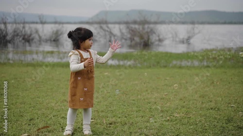 slow motion of happy toddler girl playing soap bubble in grass field near the river