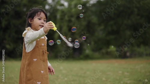 slow motion of happy toddler girl playing soap bubbles in grass field