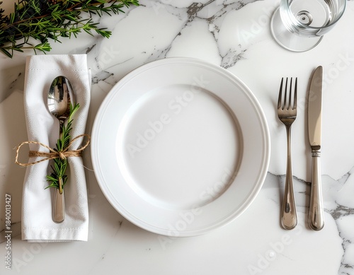 Exquisite formal place setting featuring a pristine white plate, polished silverware, and a charming rosemary garnish on a chic marble backdrop, perfect for a gourmet meal