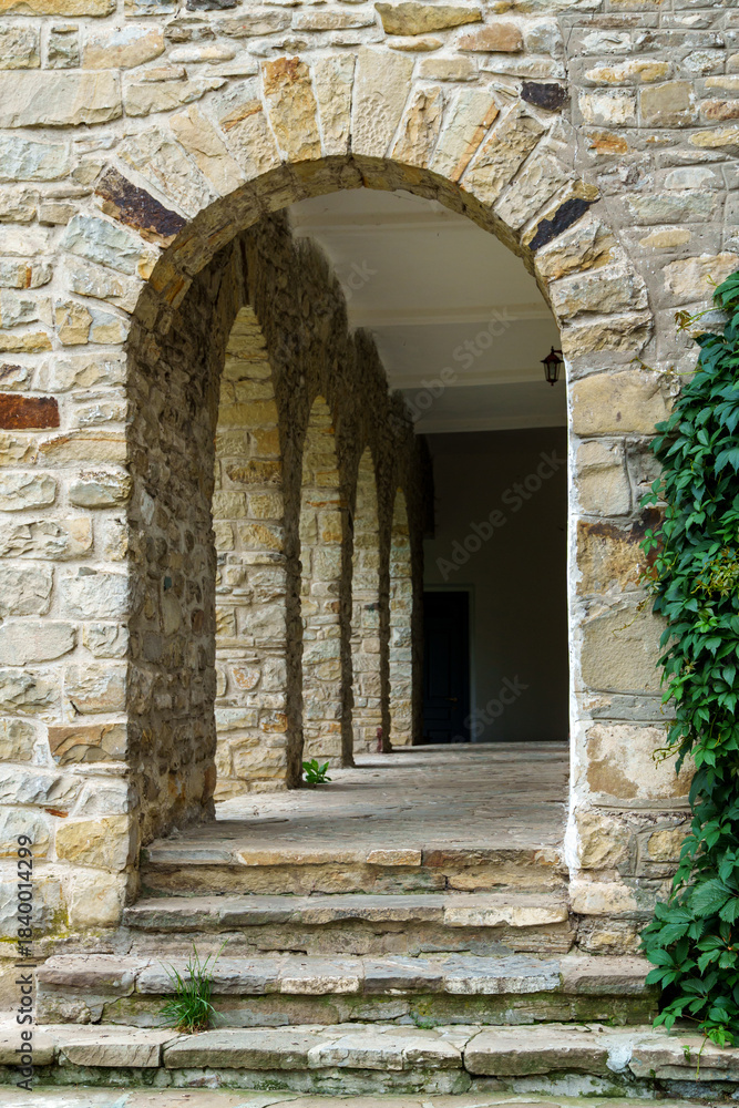 Naklejka premium close up of architectural details, old stone wall with arched opening and green ivy