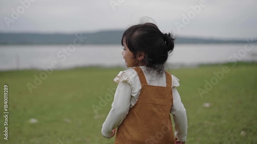 slow motion of toddler girl walking on a grass field near the river