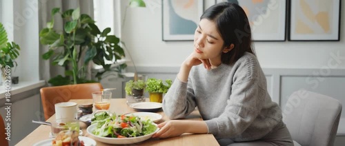 A Moment of Contemplation at the Table: A woman sits alone at a dining table, gazing at a plate of fresh salad.
