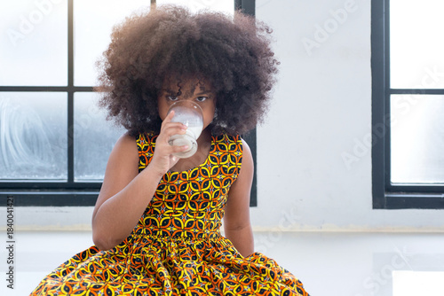 African child girl in traditional dress is drinking milk from a glass., healthy drink