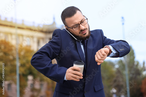 Fotografía Young businessman in suit talking on smartphone, holding takeaway coffee and che