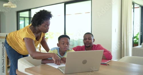 African American family tackling laptop homework at table with mother guiding son, father observing