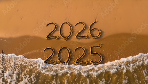 2026 Replaces 2025 Written in Beach Sand: Aerial view of numbers 2026 replacing 2025 as waves wash ashore, symbolizing time, transition, and New Year celebration.