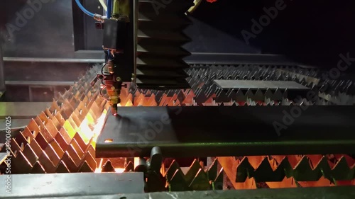 old industrial CNC laser cutting holes in sheet steel part with sparks in dark environment.