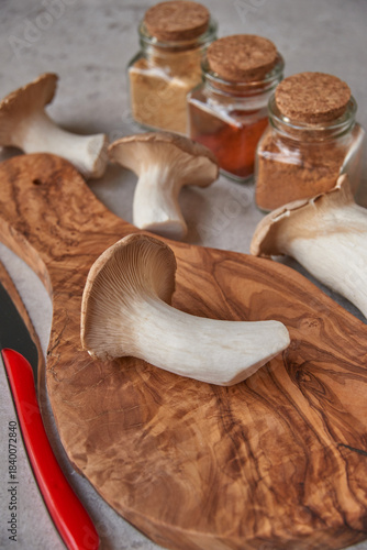 Mushrooms lying in a wooden texture board, next to it lies a knife and glass jars with a cork lid with spices