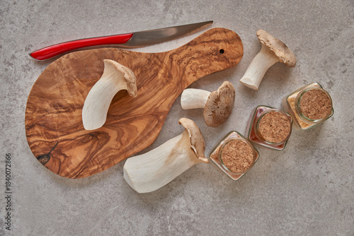 Mushrooms lying in a wooden texture board, next to it lies a knife and glass jars with a cork lid with spices