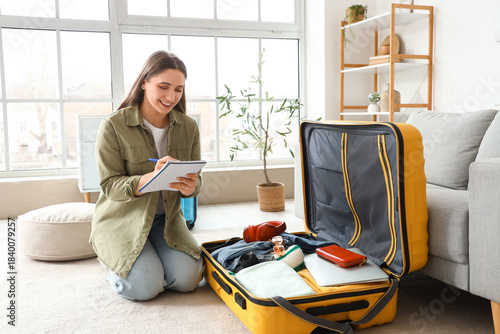Fotografie Female tourist making checklist while packing suitcase at home