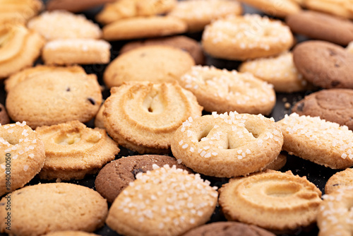 Close-up view of assorted Danish butter cookies, including sugar-topped, swirl, pretzel-shaped, and plain butter varieties. arranged to showcase their texture, golden color, and crumbly surface.