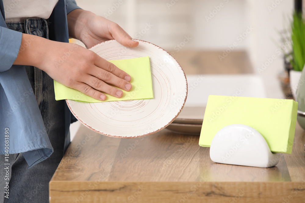Obraz premium Woman wiping plate with green paper napkin at kitchen counter