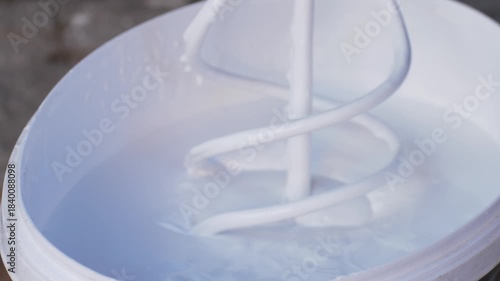 Mixer tool lowers into white paint, mixing for correct texture before use on surfaces. This ensures paint is evenly applied on walls during renovation of apartments or construction of new buildings